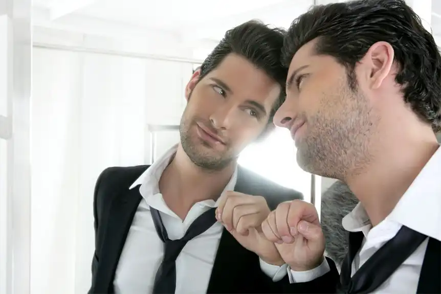 A man holding a poorly clenched fist up to a mirror, looking at himself in the eye.